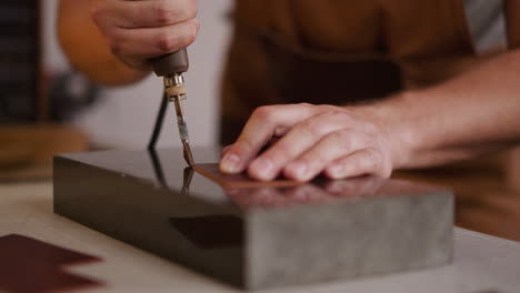 master processes leather piece edge with tool at workplace