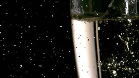 Animation-of-confetti-over-champagne-pouring-into-glass-on-black-background