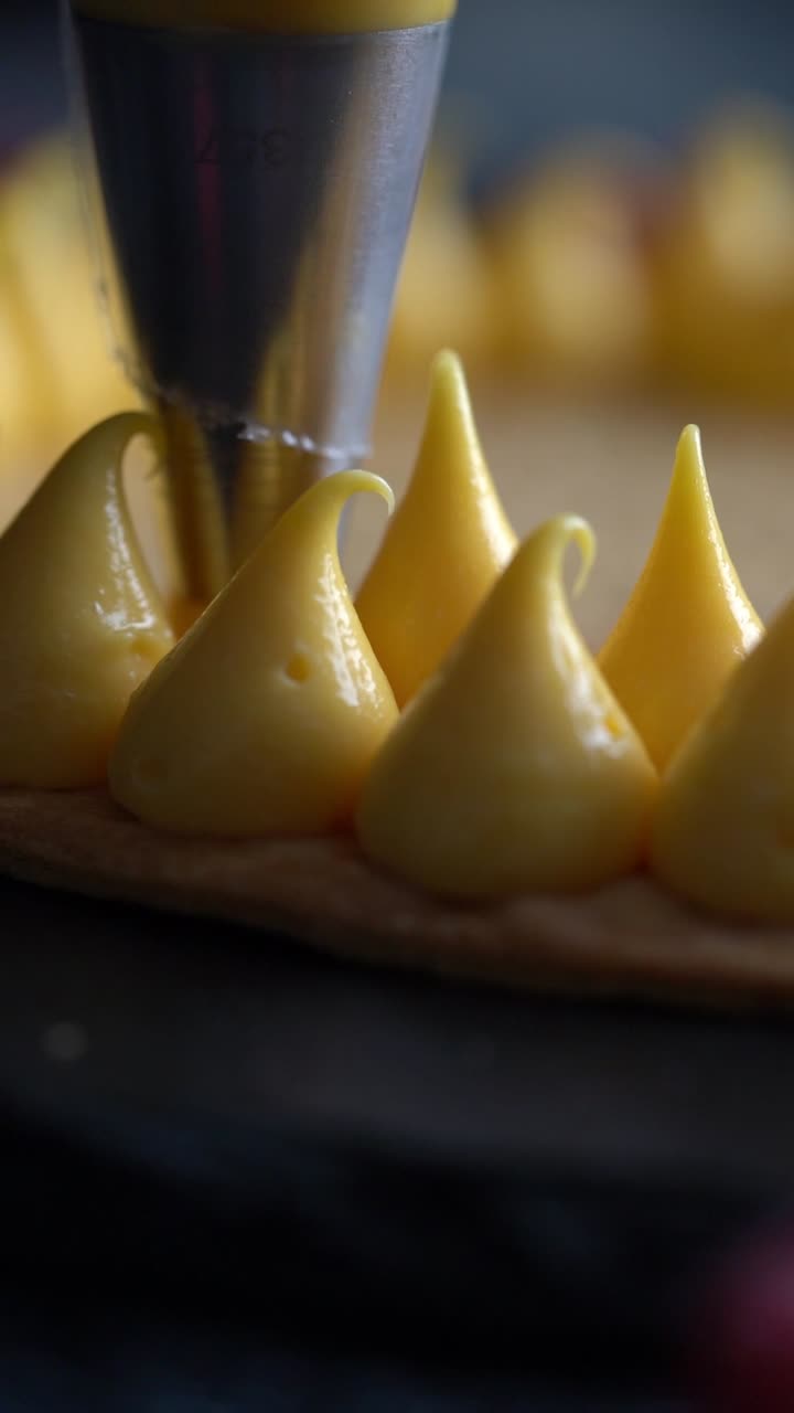 Primo piano di un pasticcere che decora una tartelletta con crema gialla