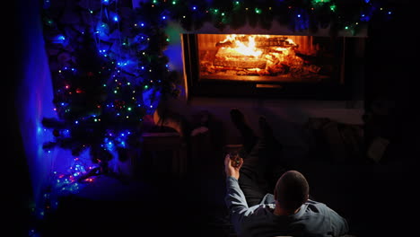 a man with a glass of spirits sits by the fireplace decorated for christmas