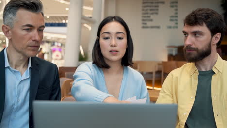 Un-Equipo-De-Trabajo-Discutiendo-Resultados-Financieros-En-Una-Laptop-En-Una-Reunión-En-Una-Cafetería