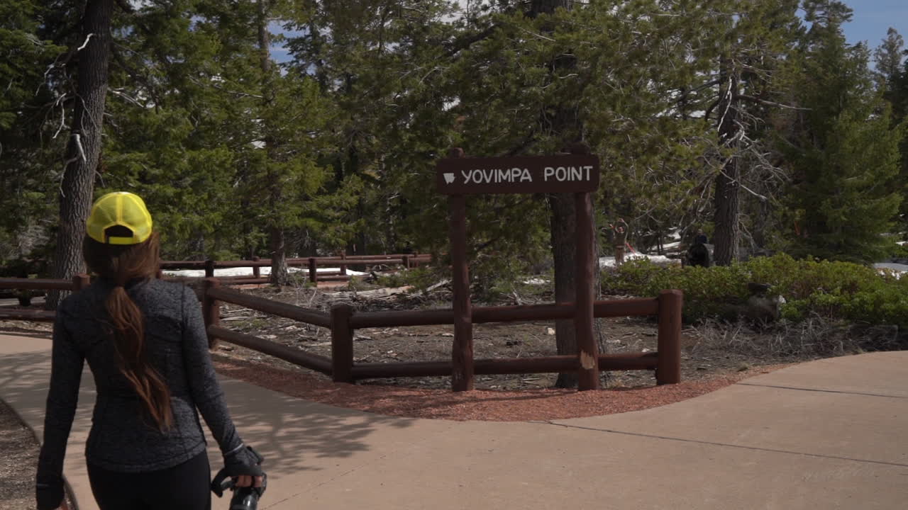 유타 주 브라이스 캐니언 국립 공원 에 있는 요빈파 포인트 절벽 과 전망대 가 있는 길 에서 카메라 를 들고  ⁇ 고 있는 여성 사진작가