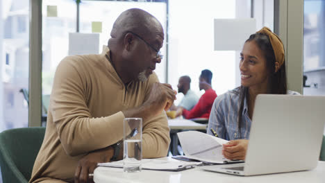 Diverse-male-and-female-business-colleagues-talking-and-using-laptop-in-office