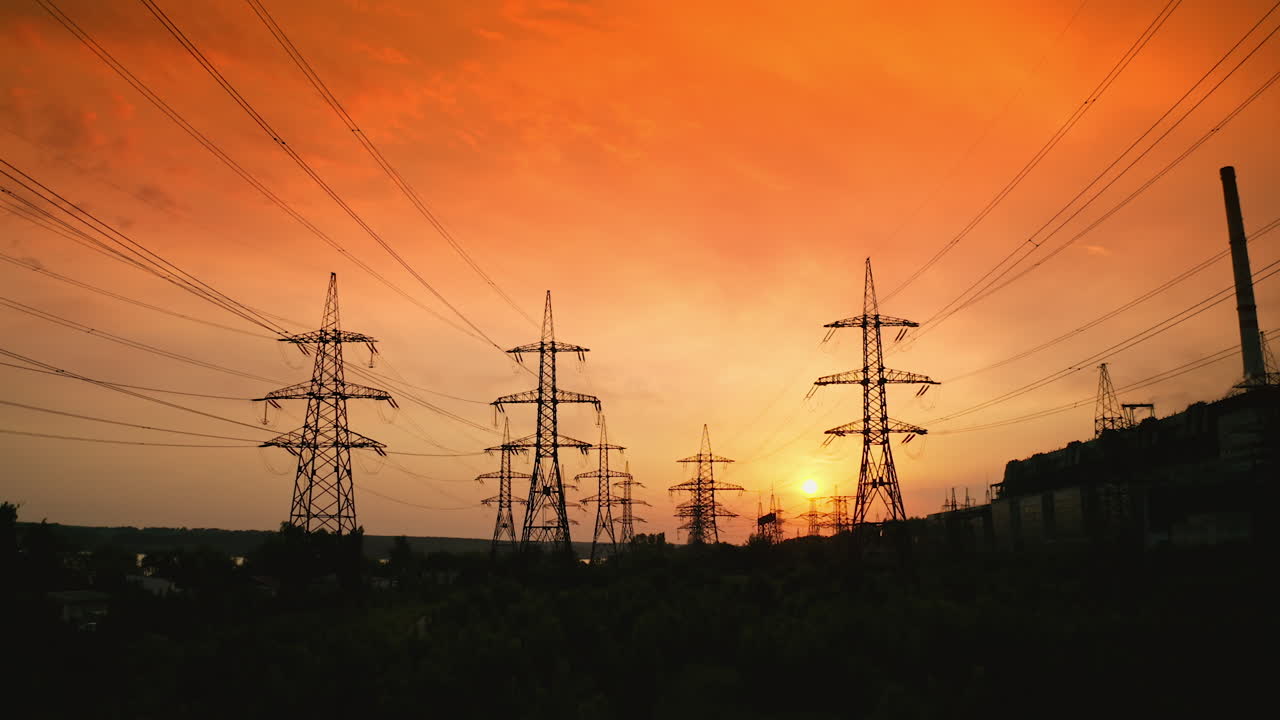 Transmission lines against red evening sky. High-voltage electricity towers at sunset. Silhouettes of electricity pylons and cables at beautiful orange sunset. Motion camera back.