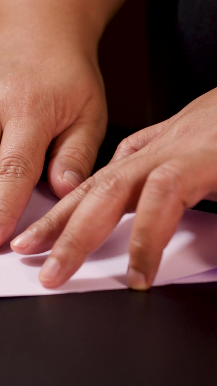 Adult hands carefully fold white paper into an origami boat, close-up, warm indoor lighting