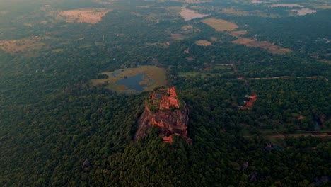 cinematic aerial drone footage flying over sigiriya rock fortress at sunrise, with a stunning backdrop of lush jungle and distant lakes shimmering in the morning light.
