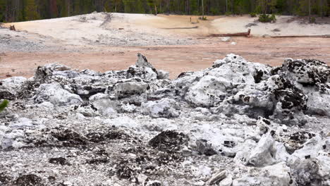 Pan-across-rock-formations-covered-with-dark-lichen-and-a-steaming-fumarole-in-background-at-Yellowstone-National-Park