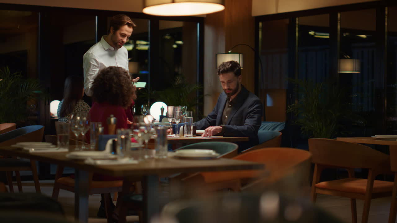 밤에 레스토랑에서 저녁을 주문하는 커플. 데이트 중인 두 연인을 서비스하는 웨이터.