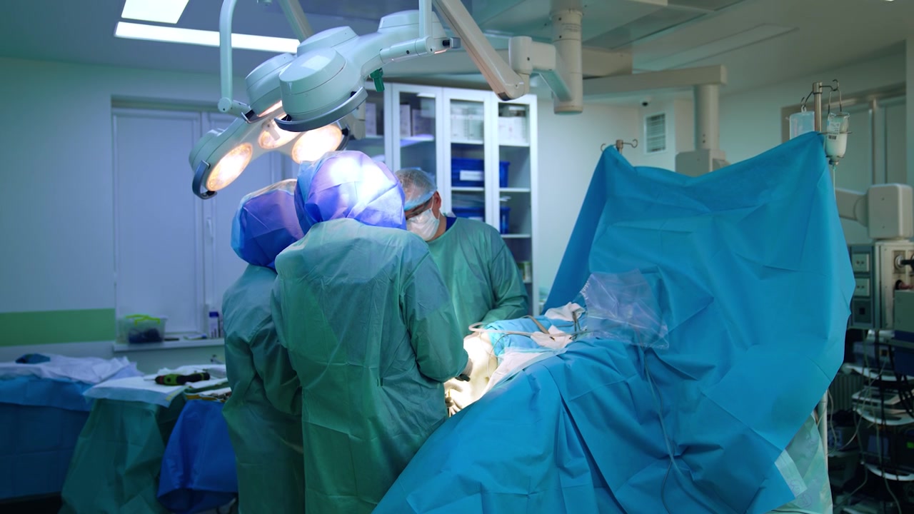 Vista posteriore di due chirurghi che collaborano mentre eseguono un intervento di chirurgia traumatologica. I medici indossano caschi protettivi durante la procedura