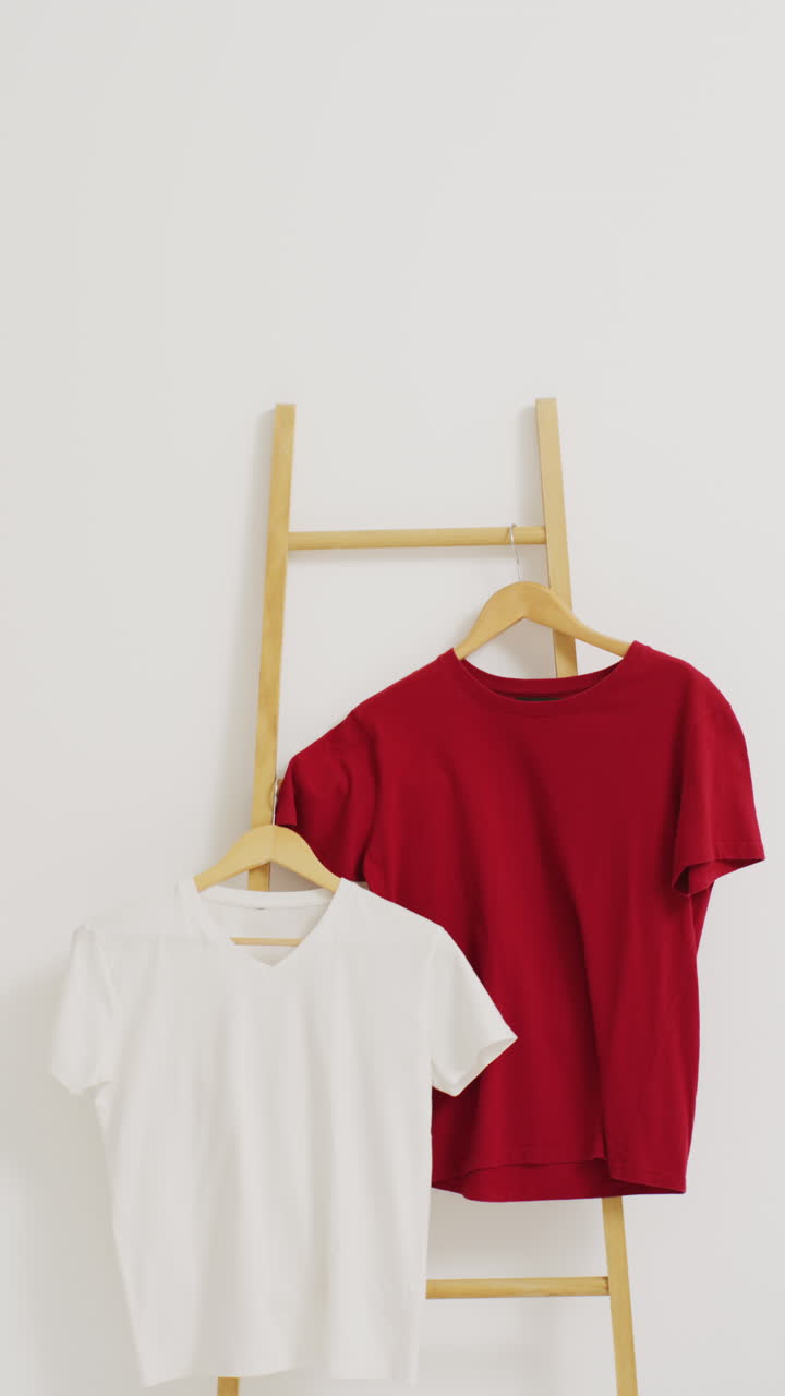 Vertical video of close up of white and red t shirts hanging from ladder with copy space