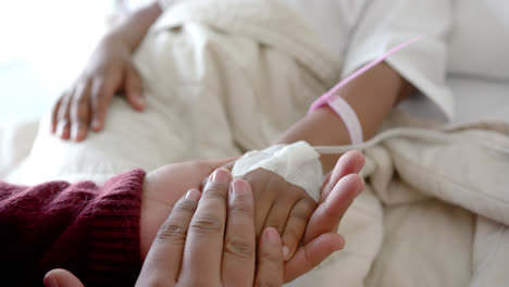 teniendo las manos de una madre y una hija afroamericanas acostadas en una cama de hospital, en cámara lenta.