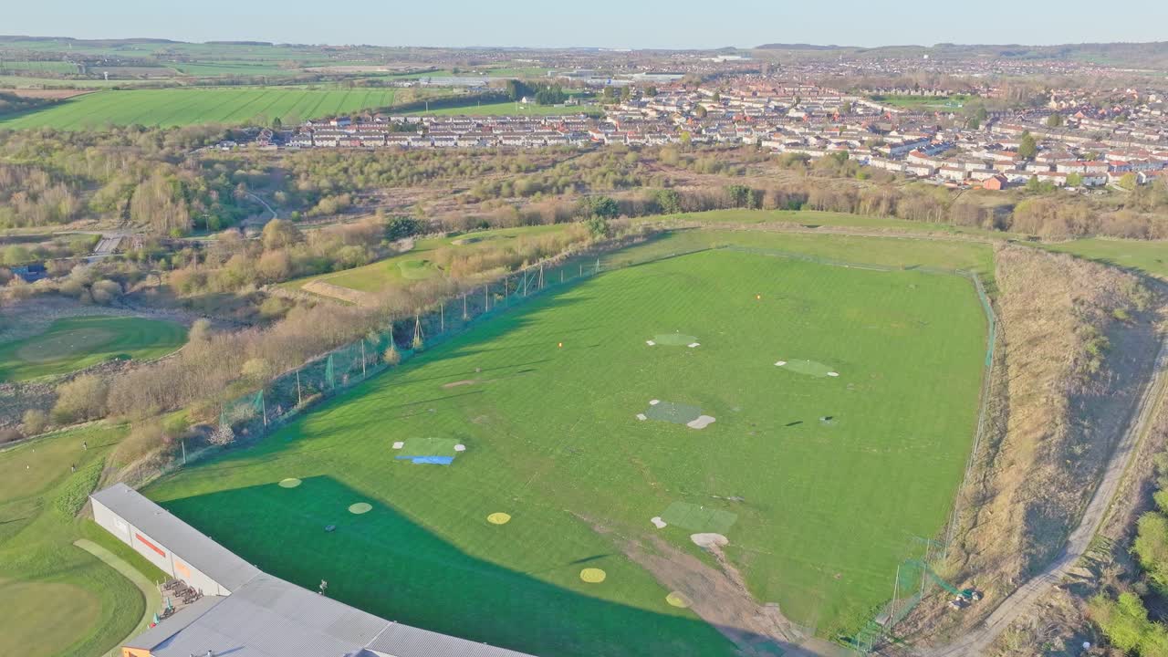 High aerial of Waterfront Golf Club driving range, Rotherham, UK, in summer morning light with suburban homes in background