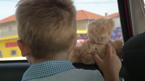 little child with teddy bear looking out car window