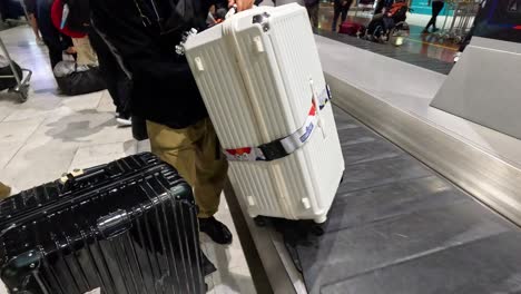 person retrieves their suitcase from a moving conveyor.