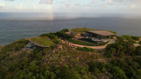 Aerial-View,-Villa-Mansion-With-Green-Roof-and-Rainbow-Above-Caribbean-Sea