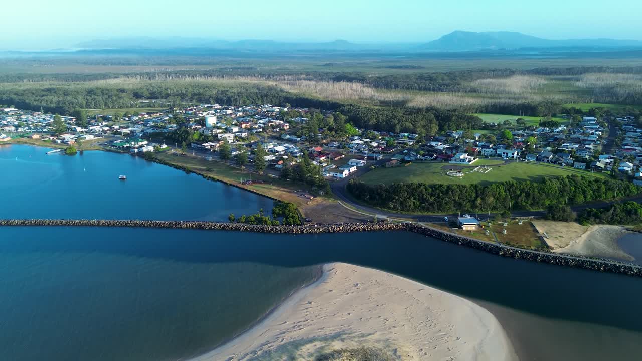 Drone aerial landscape of Harrington break wall waterfront foreshore showing rural suburban town housing river inlet and sandy dunes along bushland coastline near Taree NSW Australia travel tourism