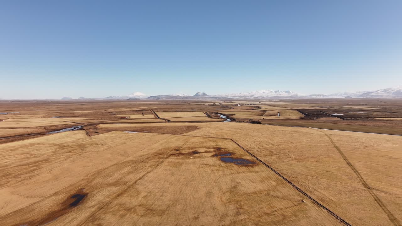 Drone flies over Iceland’s Þjórsá river plain, golden fields, winding rivers and majestic snowy peaks.