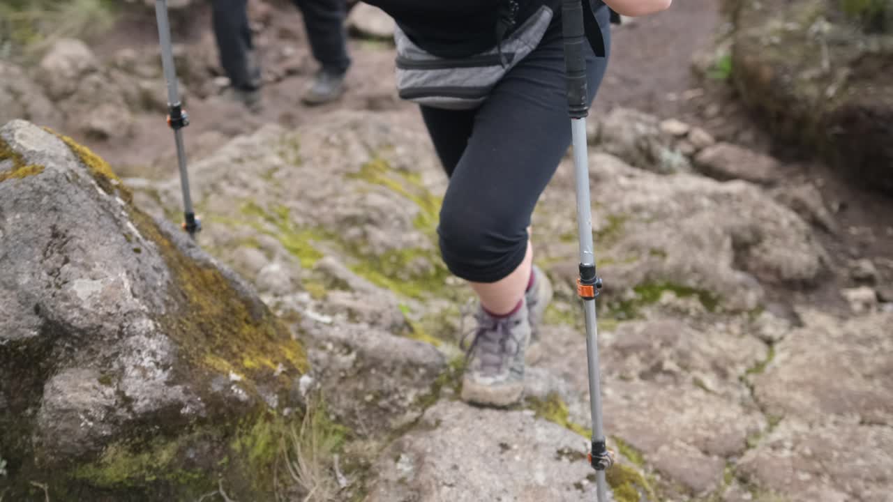 Legs of a girl walking on a trail with a backpack, action camera and trekking poles