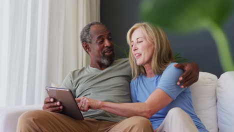 Älteres-Paar-Gemischter-Abstammung-Nutzt-Digitales-Tablet,-Während-Es-Zu-Hause-Auf-Der-Couch-Sitzt