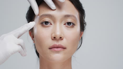회색 배경에 있는 아시아 여성의 얼굴을 만지는 장갑을 입은 손, 슬로우 모션