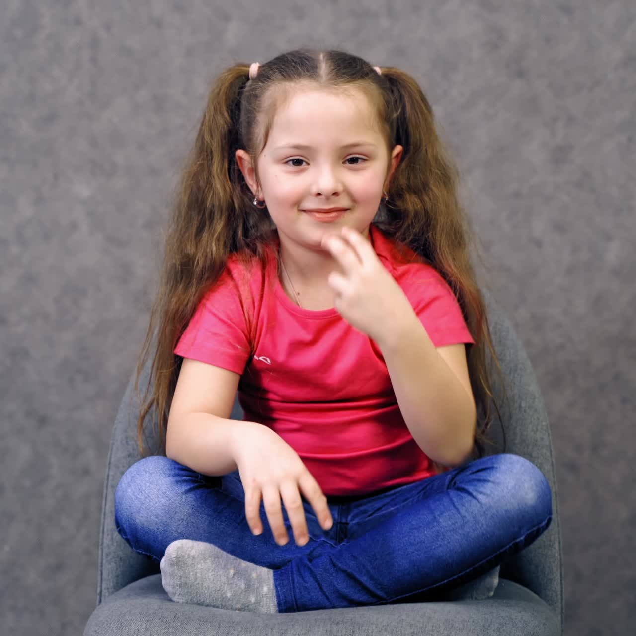 Portrait of a cute little girl sitting on chair. Happy adorable small girl looking forward and showing her fingers at camera.