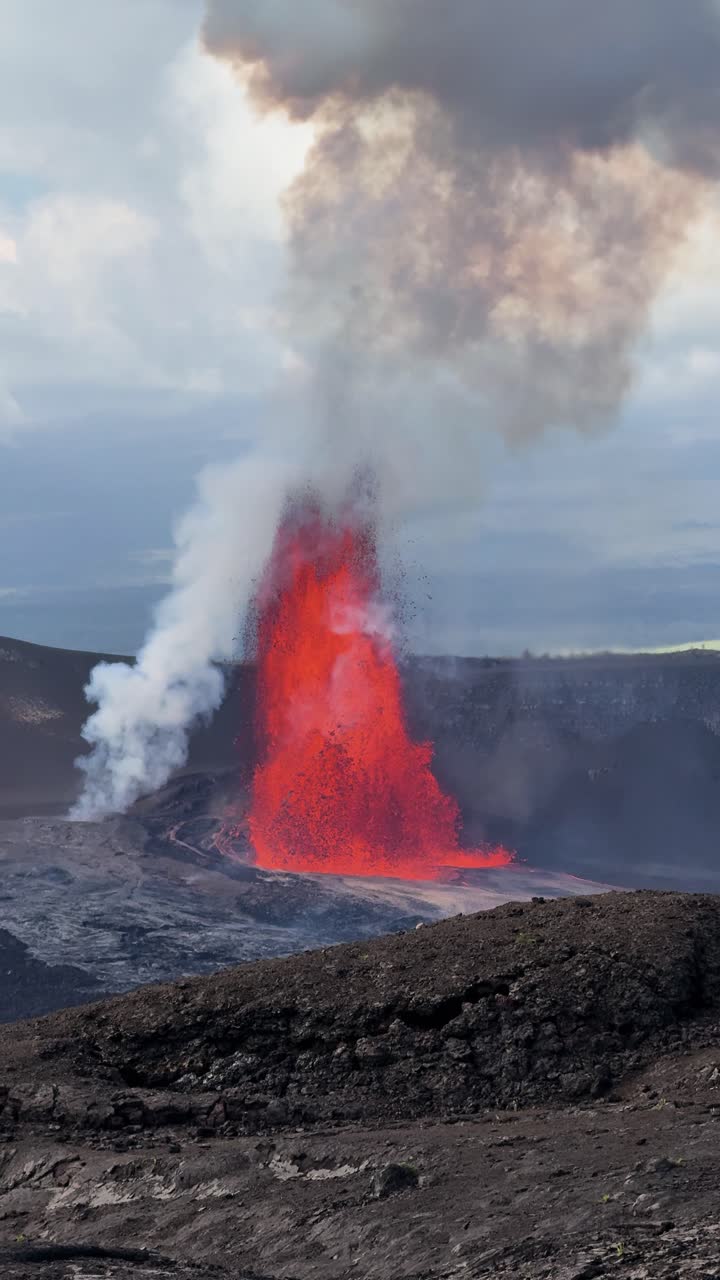 Vertical close up of powerful lava fountain at Kīlauea volcano, Big Island Hawaii, showing glowing magma and thick smoke rising from crater