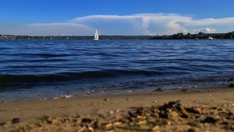 Low-angle-pov-from-shore-of-small-boat-sailing-in-calm-open-lake-waters-of-Maggiore-lake-in-Italy