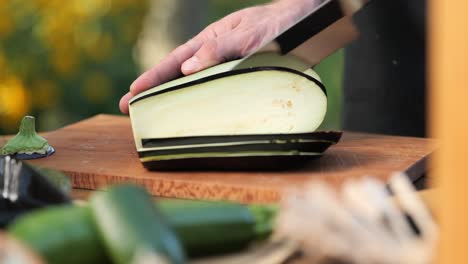 Young-man-cutting-aubergine-on-a-wooden-board-in-his-garden-close-up