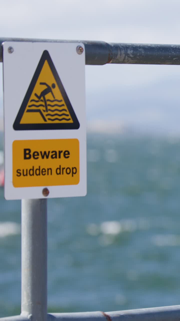 Close-up of warning sign on coastal barrier, windy seaside, bright daylight, slight camera movement
