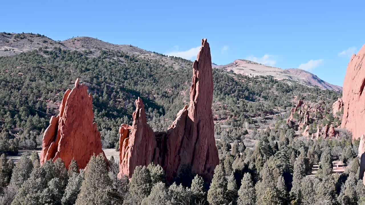 Aerial view of jagged red sandstone hoodoos rising from a dense forested landscape with rolling hills in Garden of the Gods, Colorado