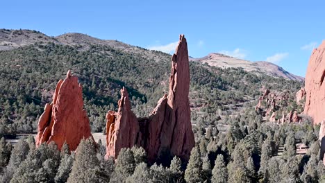 aerial view of jagged red sandstone hoodoos rising from a dense forested landscape with rolling hills in garden of the gods, colorado
