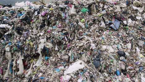 Drone-shot-of-a-landfill-with-trucks-and-tractors-managing-garbage,-highlighting-waste-disposal-and-recycling-efforts