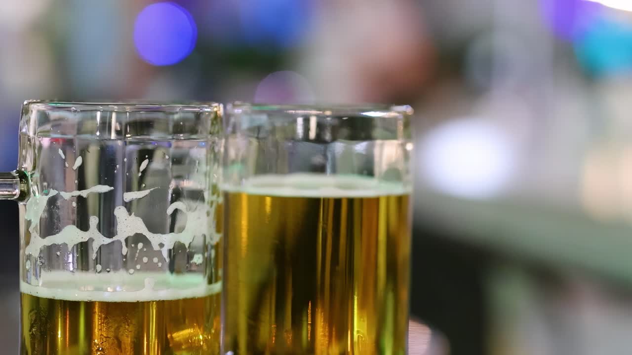 Two clear beer mugs filled with golden liquid, set against a colorful bokeh background.