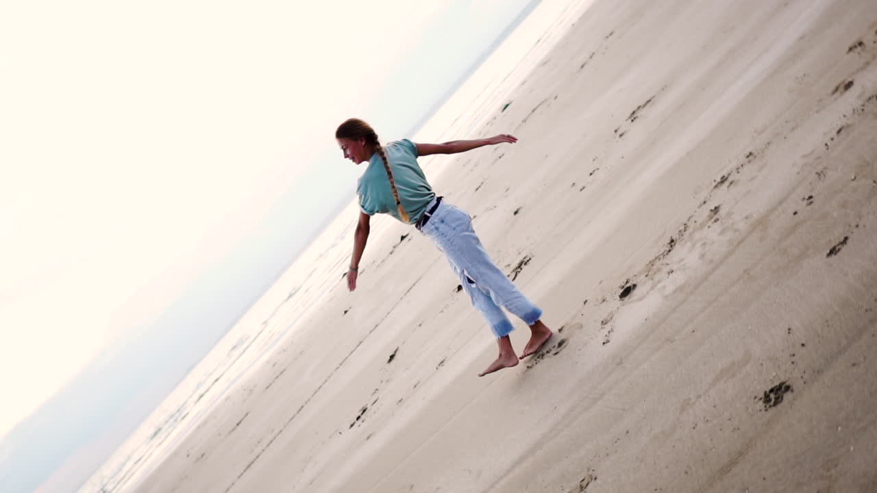 머리에 긴 머리를 하고 운동복을 입고 수레바퀴를 하고 해변에서 회전하는 행복한 금발 소녀