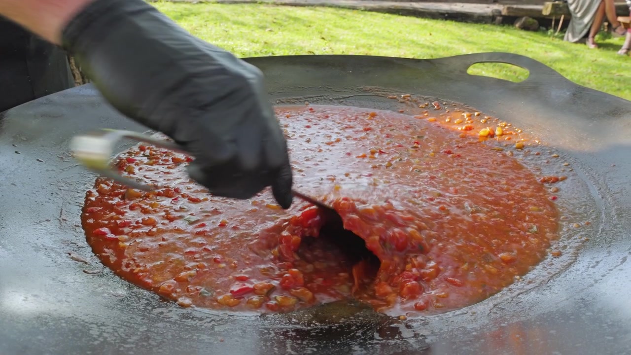 Preparazione di un sugo di verdure tradizionale locale per la pasta in una grande padella all'aperto su un fuoco. Lo chef mescola il sugo al rallentatore. Cucina italiana.