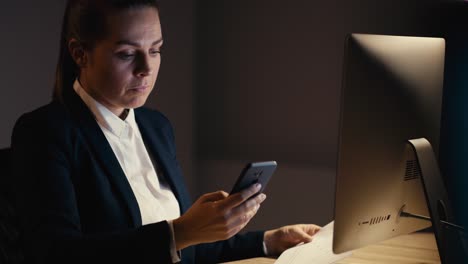 mujer de negocios caucásica que trabaja hasta tarde en la oficina y usa el teléfono móvil