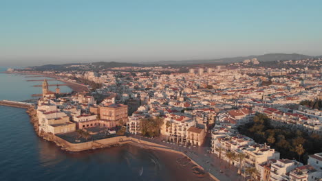 Coastal-cityscape-drone-perspective-during-golden-hour-with-buildings,-sea,-mountains