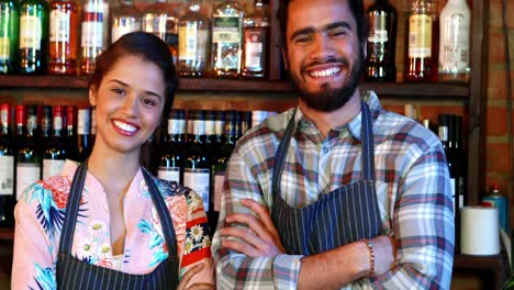 portrait of barmaid and barman standing with arms crossed at bar counter