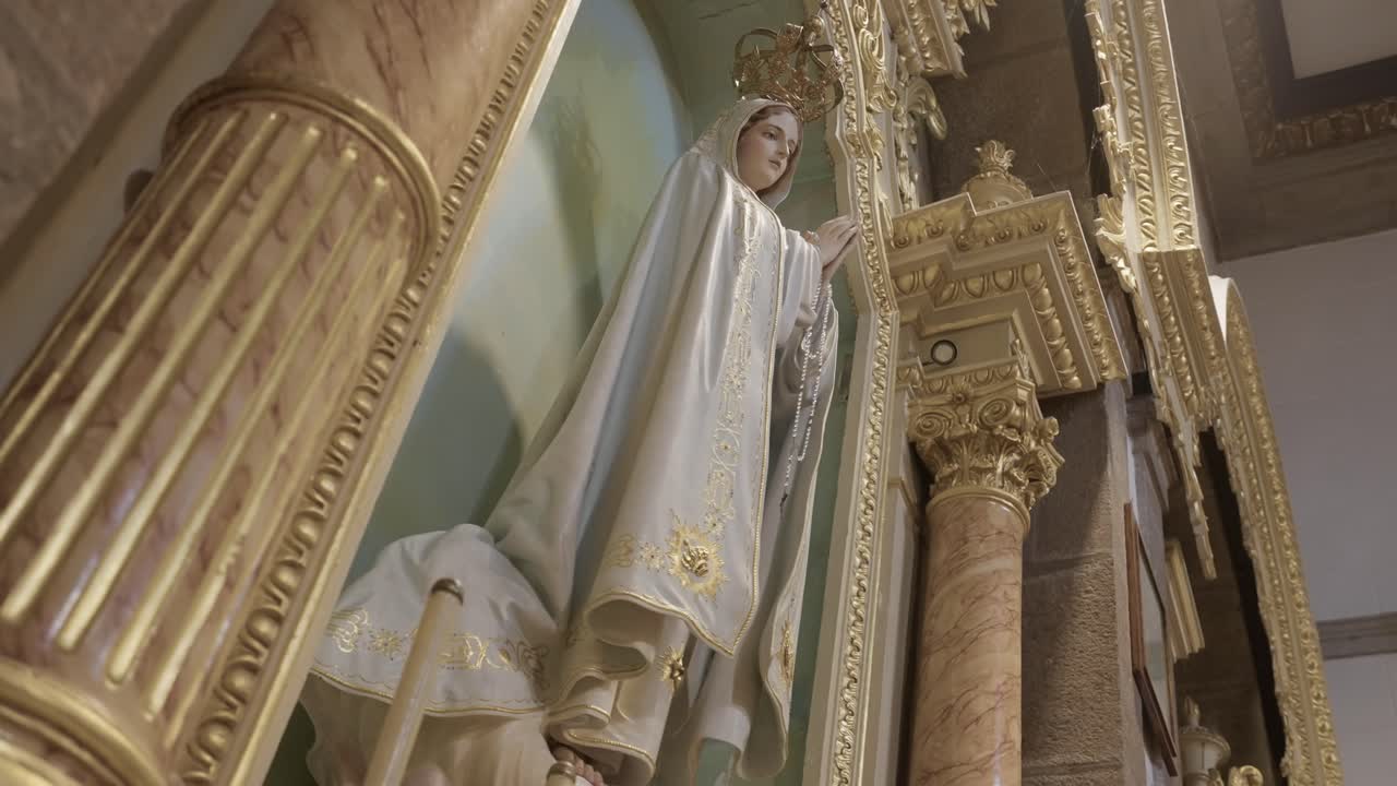 Nahaufnahme einer Statue der Jungfrau Maria, umrahmt von goldenen Säulen im Inneren einer Kirche