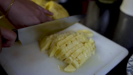 cerca de manos cortando piña amarilla en una tabla para cortar
