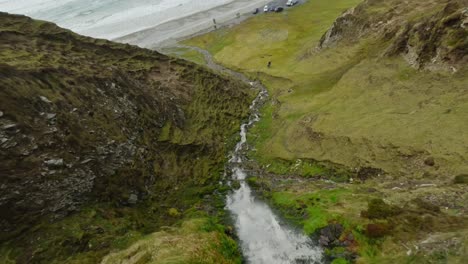 drone buceando por una pequeña cascada en acantilados verdes hacia la playa de la quilla en irlanda