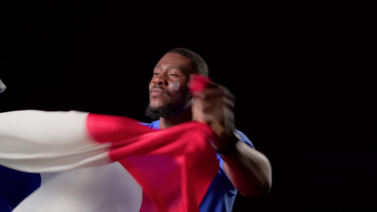 Hombre africano adulto levantando y ondeando una bandera tricolor tras haberla colocado, celebrando la victoria en el estudio.