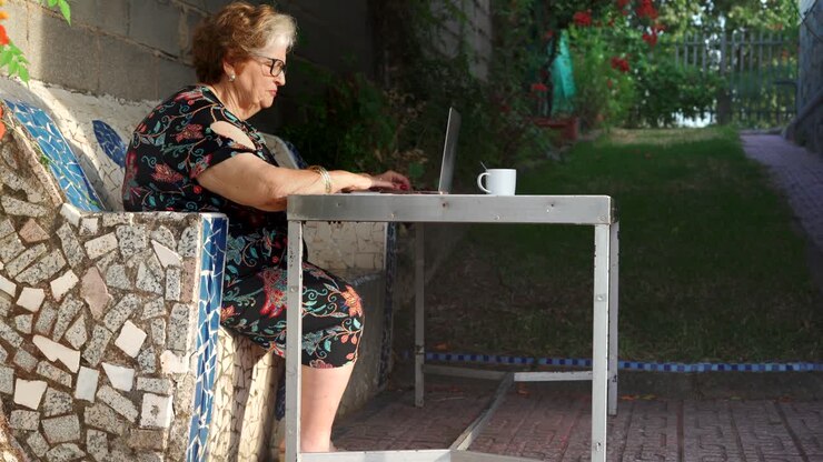 una mujer envejecida sonriente usando una computadora portátil en la mesa en el jardín