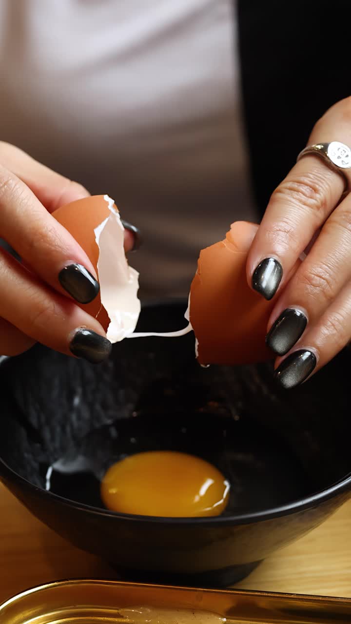 Closeup female hands crack raw egg into black bowl under warm restaurant-style lighting