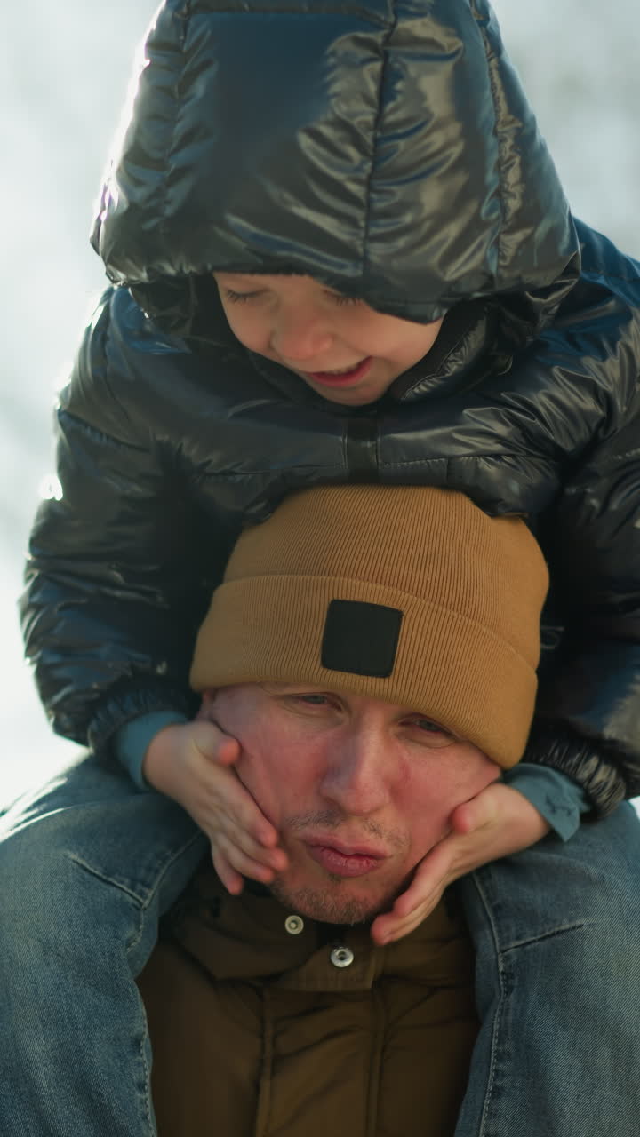 아들이 장난스럽게 을 고 웃는 동안 아들을 어깨에 고 있는 아버지, 아빠는 그 순간을 즐기고 있는 것처럼 보이며, 뒤에서 부드러운 빛이 비추고 있다.