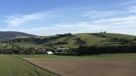 toma aérea panorámica de 4k de un pequeño pueblo en verano en medio de un campo de hierba en dolní morava, república checa, bajo una colina con árboles y un cielo azul arriba