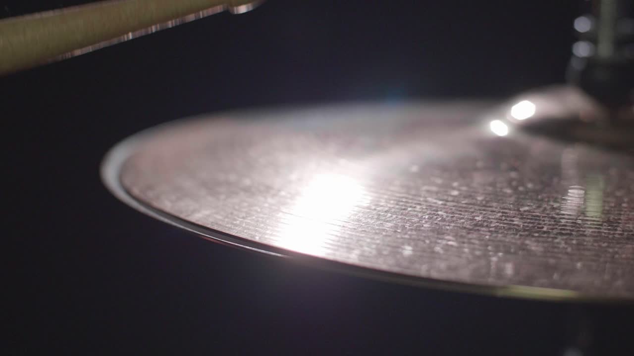 Smooth close up of a drum hi-hat being played with sticks. Super Close up with a dark background. Gimbal panning movement. Shallow depth with fixed focus. Shot in 4K