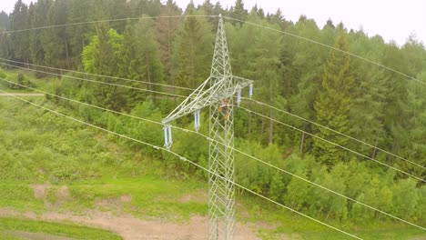 un electricista trabaja en un enorme poste eléctrico en la europa rural, con un fondo de bosque verde.