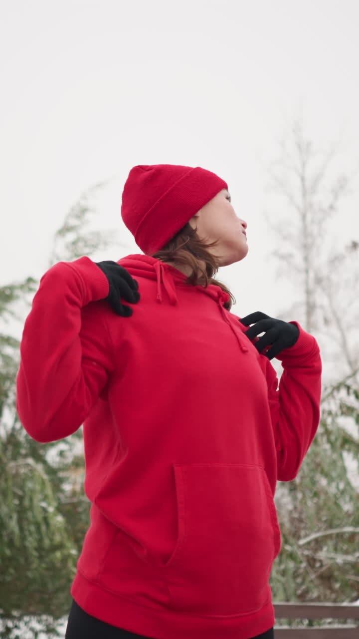 lady performing hand stretch by turning arm in fitness routine outdoors, dressed in athletic wear, snow-covered ground, frosted trees, and bench in serene park setting, winter workout