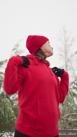 lady performing hand stretch by turning arm in fitness routine outdoors, dressed in athletic wear, snow-covered ground, frosted trees, and bench in serene park setting, winter workout